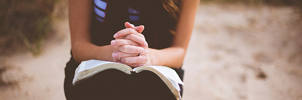 Illusztráció. Egy lány imádkozik szép napsütésben egy Bibliával a kezében. 